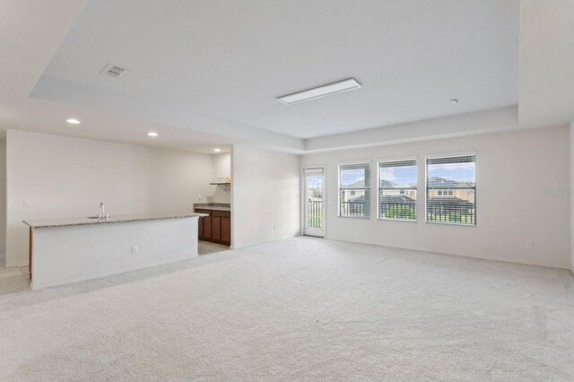 unfurnished living room featuring a raised ceiling, light carpet, and sink