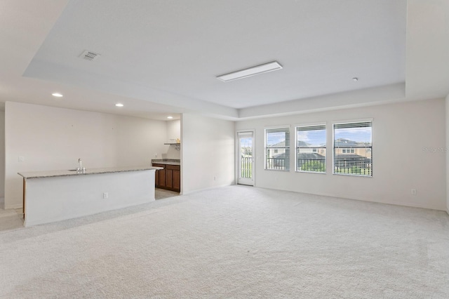 unfurnished living room with visible vents, light carpet, a tray ceiling, and recessed lighting