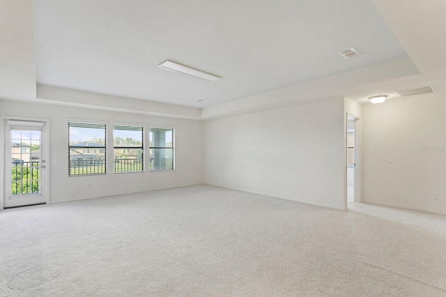 spare room featuring light carpet, visible vents, and a raised ceiling