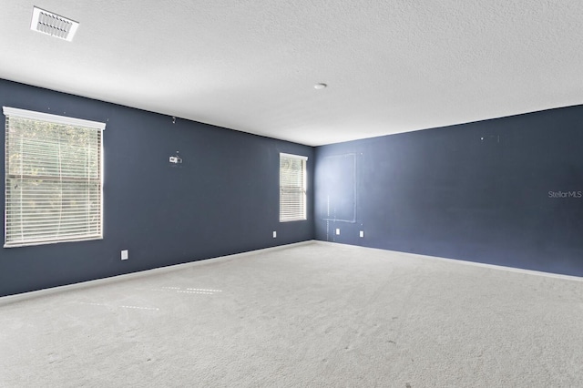 spare room featuring plenty of natural light, visible vents, carpet flooring, and a textured ceiling