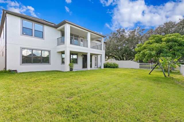 back of property featuring a balcony, a lawn, stucco siding, and a fenced backyard