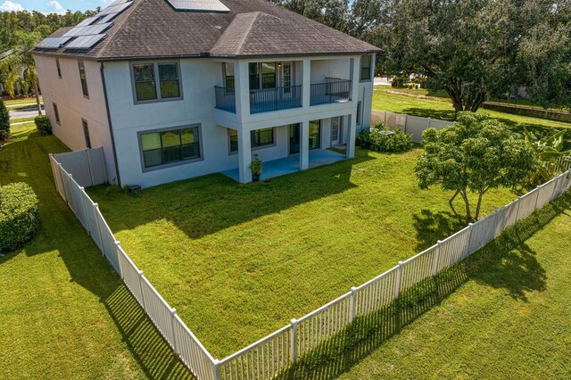 back of property featuring solar panels, a balcony, a yard, and a patio