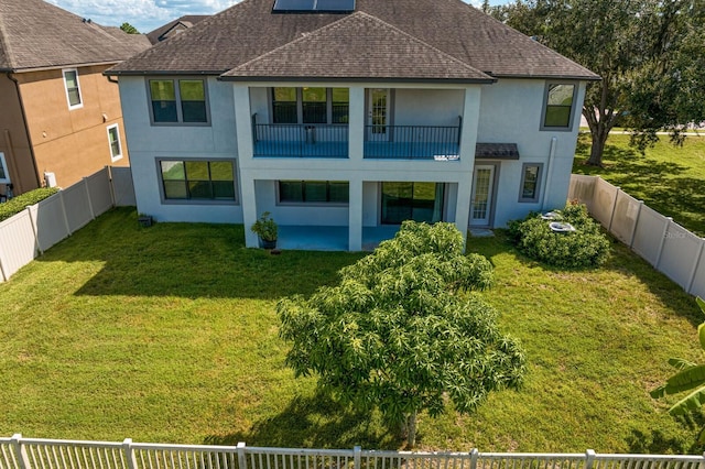 back of property featuring a balcony, a fenced backyard, stucco siding, a shingled roof, and a yard