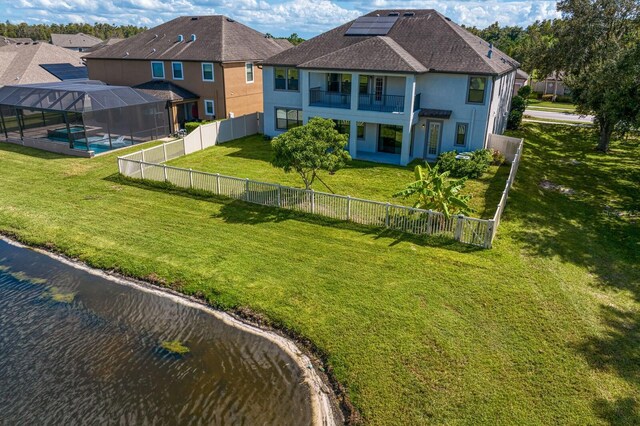 back of house featuring stucco siding, a fenced backyard, a balcony, a yard, and roof mounted solar panels