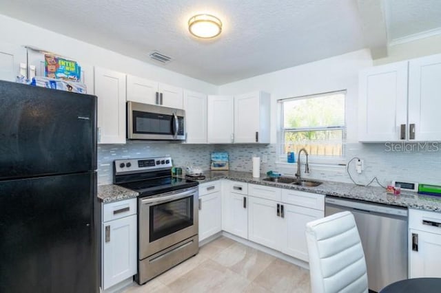 kitchen with light stone counters, stainless steel appliances, sink, and white cabinetry