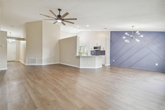 unfurnished living room with a textured ceiling, light hardwood / wood-style flooring, high vaulted ceiling, and ceiling fan with notable chandelier