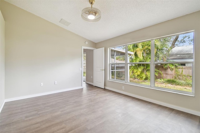 spare room with hardwood / wood-style floors, a textured ceiling, and lofted ceiling