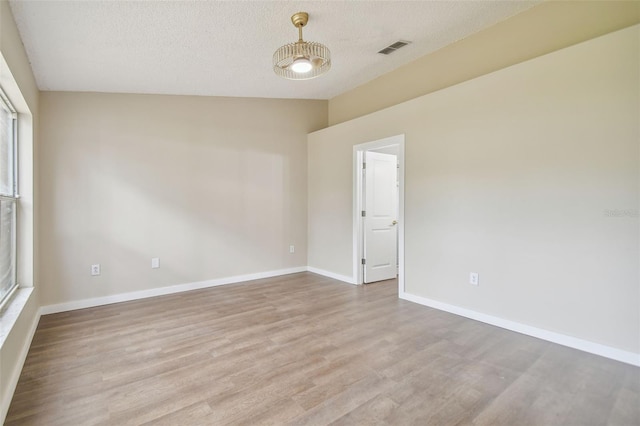 spare room featuring a textured ceiling, light hardwood / wood-style floors, and lofted ceiling