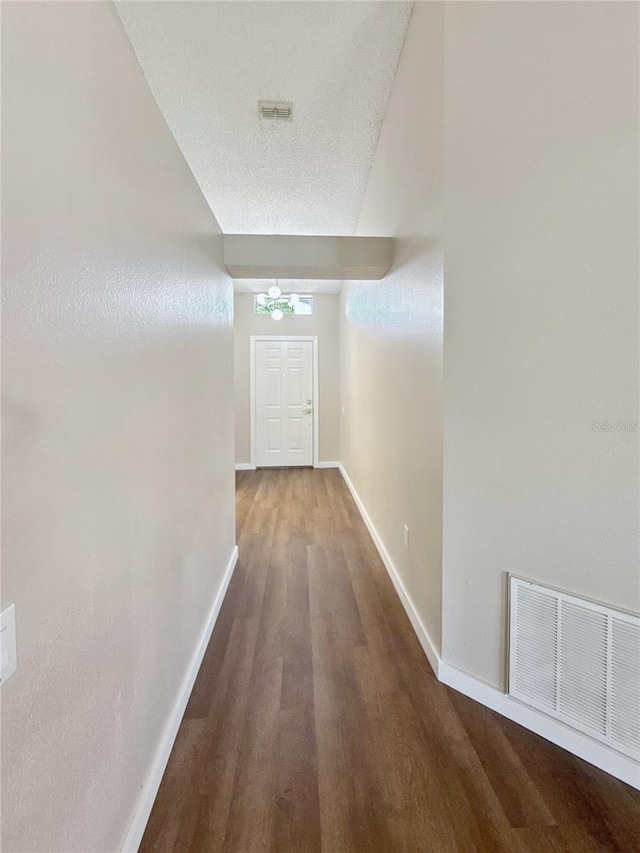 hall featuring a textured ceiling, wood finished floors, visible vents, and baseboards