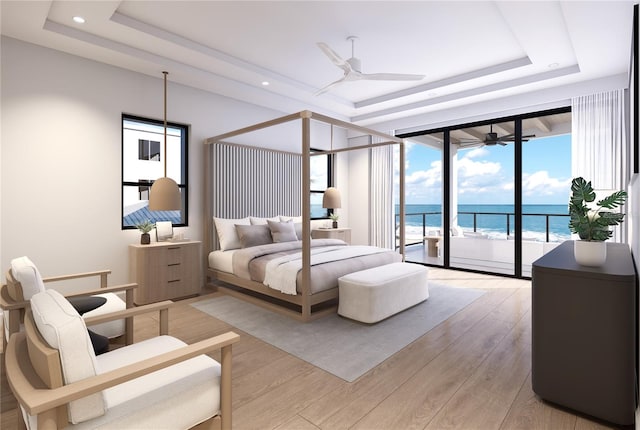 bedroom with light wood-type flooring, a water view, a tray ceiling, and access to exterior