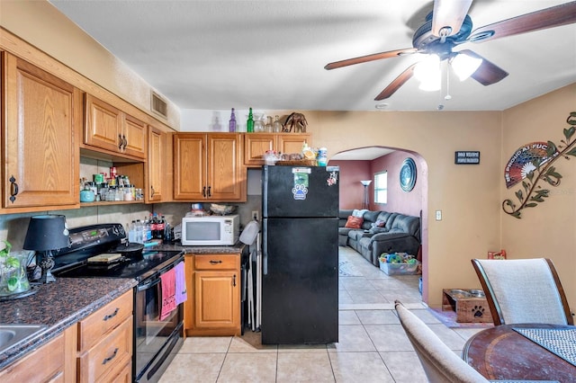 kitchen featuring dark stone counters, black appliances, light tile patterned floors, and ceiling fan