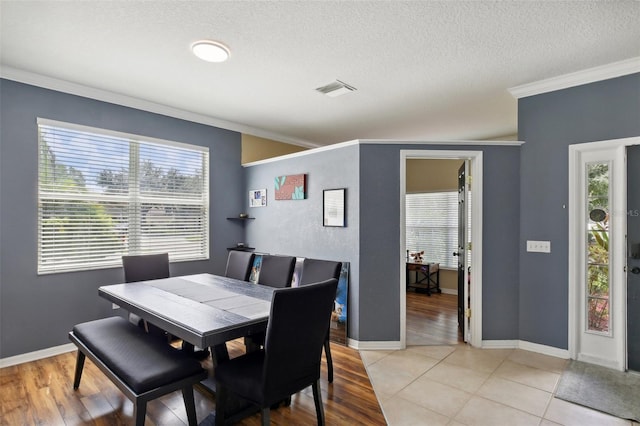 dining area featuring a textured ceiling, light wood-type flooring, and crown molding