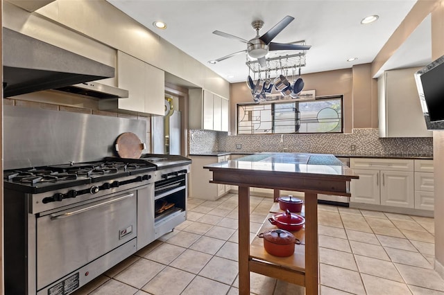 kitchen with high end stove, white cabinetry, decorative backsplash, light tile patterned floors, and ceiling fan