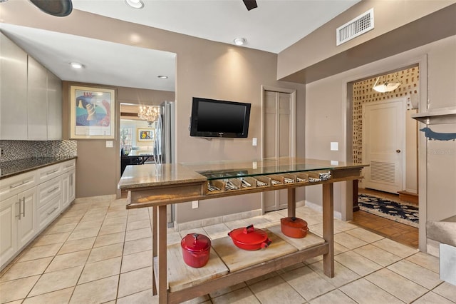 kitchen with stainless steel fridge, light tile patterned flooring, white cabinetry, and decorative backsplash