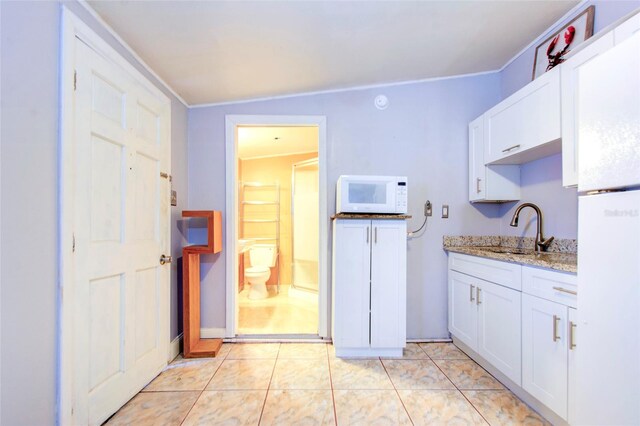 kitchen with light stone counters, white cabinets, lofted ceiling, light tile patterned floors, and sink