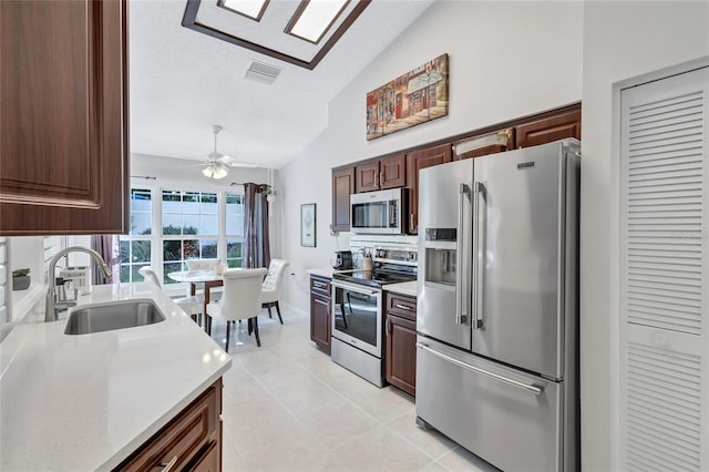 kitchen featuring sink, vaulted ceiling, appliances with stainless steel finishes, light tile patterned floors, and ceiling fan