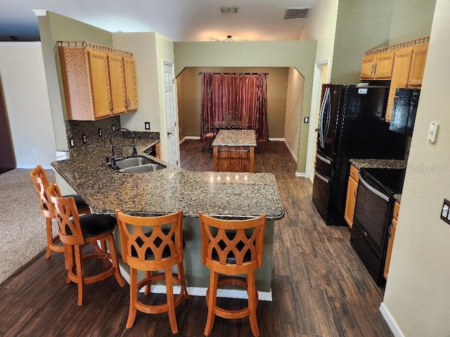 kitchen featuring kitchen peninsula, dark hardwood / wood-style flooring, a breakfast bar, black appliances, and sink