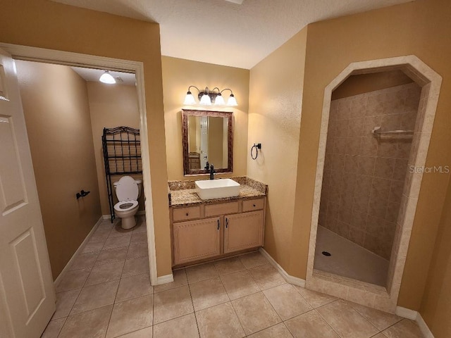 bathroom featuring a tile shower, tile patterned flooring, vanity, and toilet