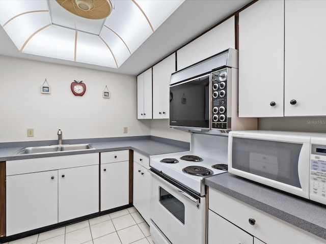 kitchen with light tile patterned floors, white appliances, a sink, and white cabinets