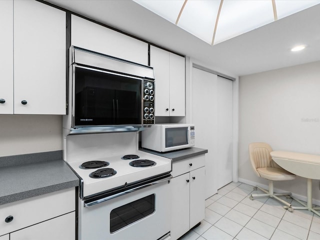 kitchen featuring light tile patterned floors, dark countertops, white cabinets, white appliances, and baseboards