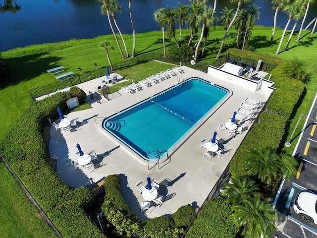 community pool with a water view, a yard, fence, and a patio