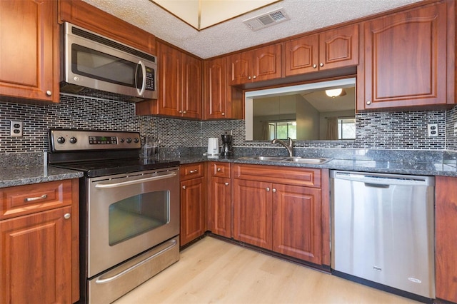 kitchen with light wood-type flooring, a textured ceiling, tasteful backsplash, sink, and stainless steel appliances