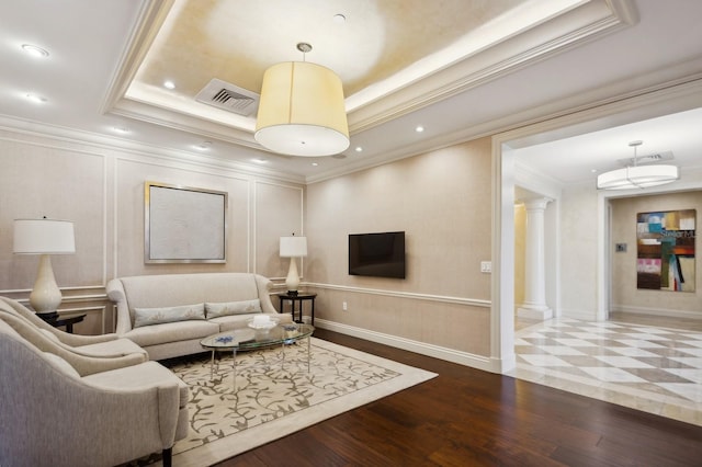 living room featuring wood-type flooring, ornamental molding, a tray ceiling, and ornate columns