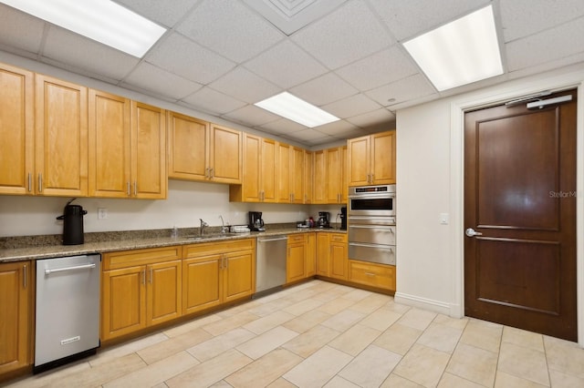 kitchen with a drop ceiling, appliances with stainless steel finishes, dark stone counters, and sink