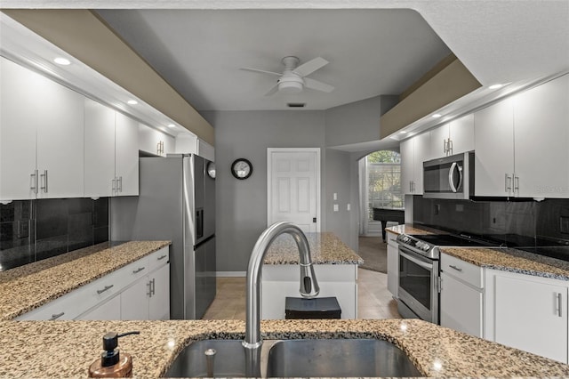 kitchen featuring ceiling fan, light stone counters, white cabinetry, stainless steel appliances, and decorative backsplash