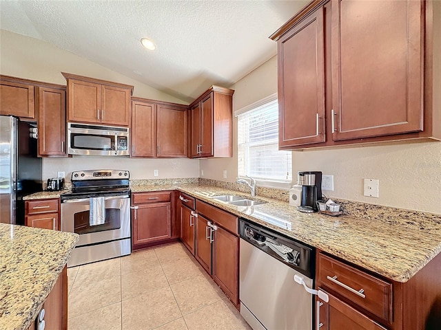 kitchen with light stone countertops, stainless steel appliances, sink, lofted ceiling, and light tile patterned flooring