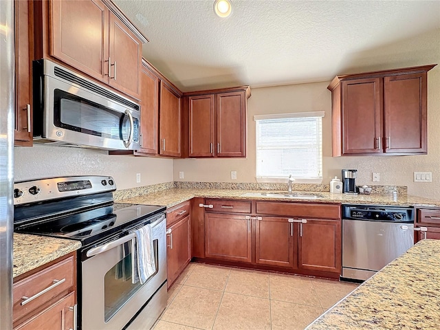 kitchen with sink, light tile patterned floors, a textured ceiling, light stone countertops, and appliances with stainless steel finishes