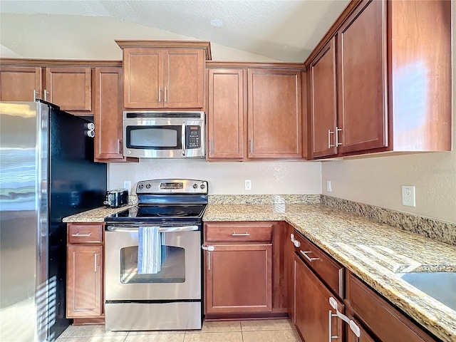 kitchen featuring light stone countertops, appliances with stainless steel finishes, light tile patterned floors, and vaulted ceiling