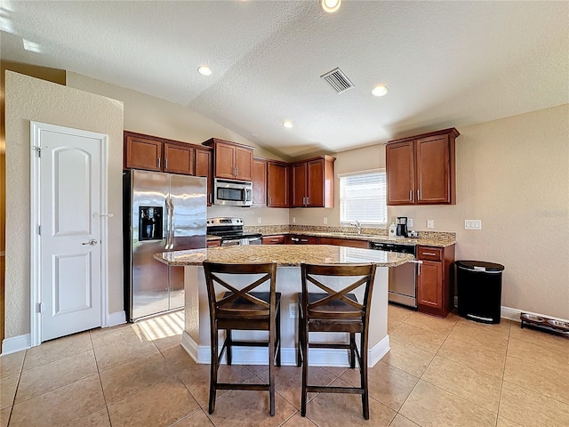 kitchen featuring sink, stainless steel appliances, lofted ceiling, a breakfast bar area, and a kitchen island