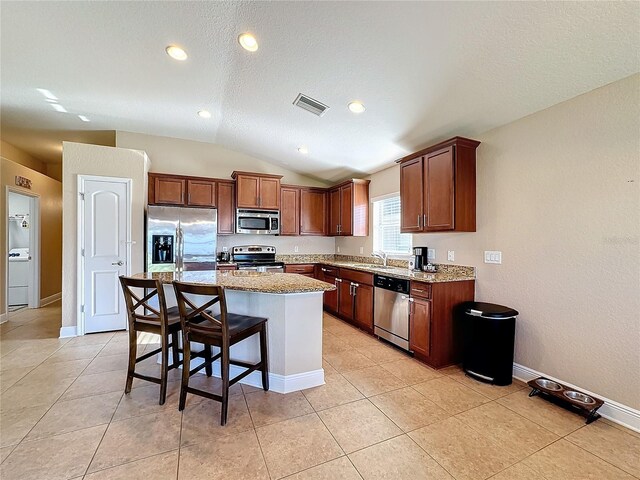 kitchen with a breakfast bar area, vaulted ceiling, light stone countertops, a kitchen island, and stainless steel appliances