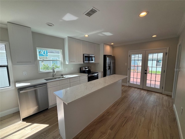 kitchen featuring appliances with stainless steel finishes, white cabinetry, dark wood-type flooring, a center island, and sink