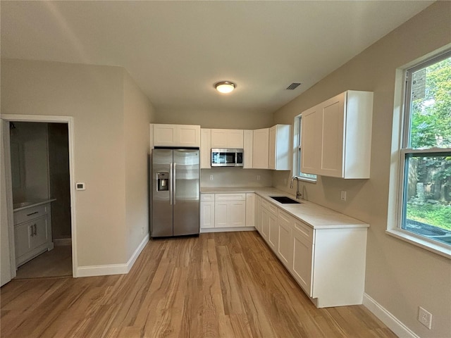 kitchen with stainless steel appliances, white cabinets, light wood-type flooring, and sink