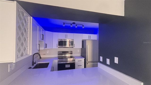 kitchen featuring stainless steel appliances, sink, kitchen peninsula, and white cabinetry