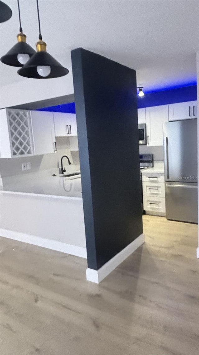 interior space featuring appliances with stainless steel finishes, white cabinetry, light hardwood / wood-style flooring, and pendant lighting