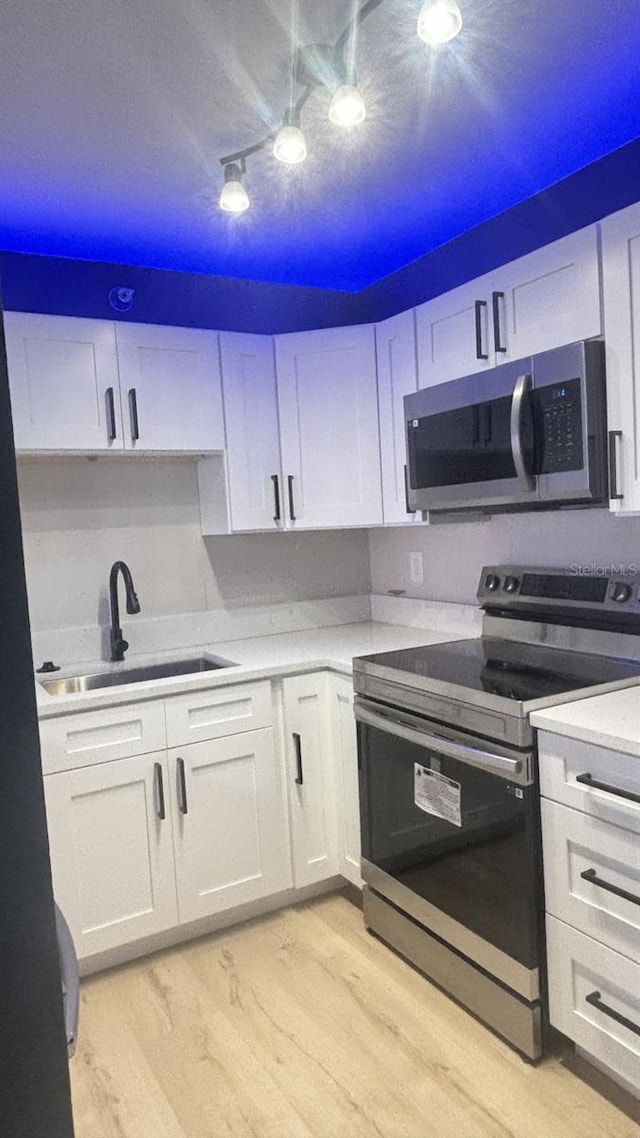 kitchen with light hardwood / wood-style floors, sink, stainless steel appliances, and white cabinets