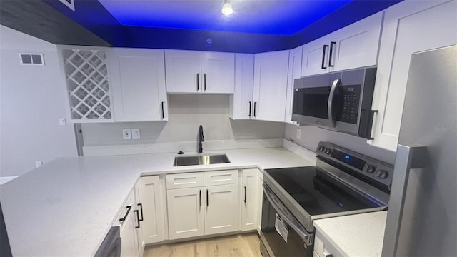 kitchen featuring sink, white cabinets, light hardwood / wood-style flooring, stainless steel appliances, and light stone countertops