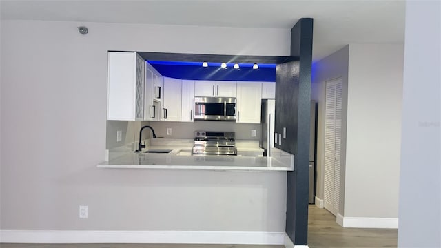 kitchen featuring wood-type flooring, sink, white cabinetry, kitchen peninsula, and stainless steel appliances