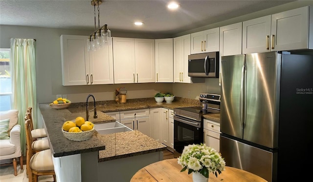 kitchen with appliances with stainless steel finishes, decorative light fixtures, sink, white cabinets, and a breakfast bar area