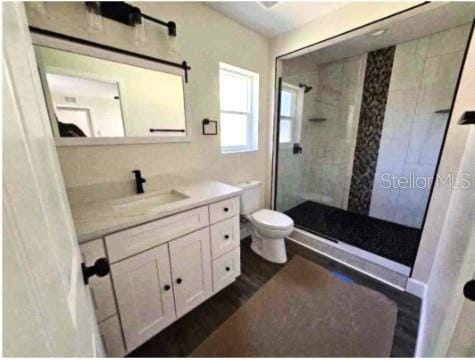 bathroom featuring tiled shower, vanity, hardwood / wood-style flooring, and toilet