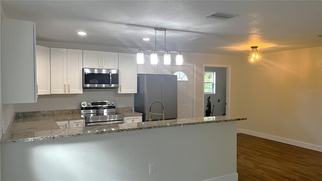 kitchen with light stone counters, stainless steel appliances, white cabinetry, dark wood-type flooring, and kitchen peninsula