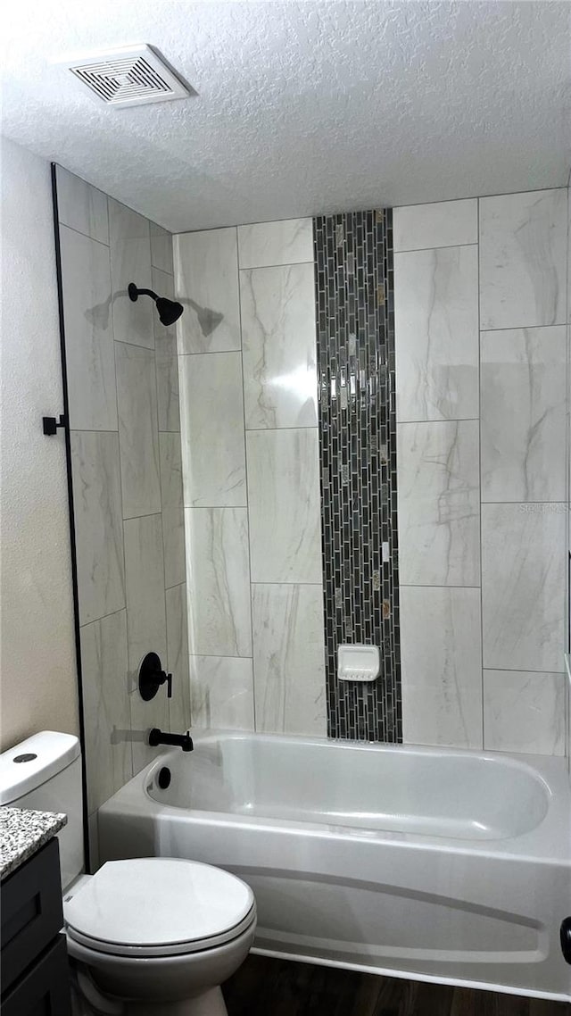 full bathroom featuring toilet, tiled shower / bath combo, vanity, and a textured ceiling