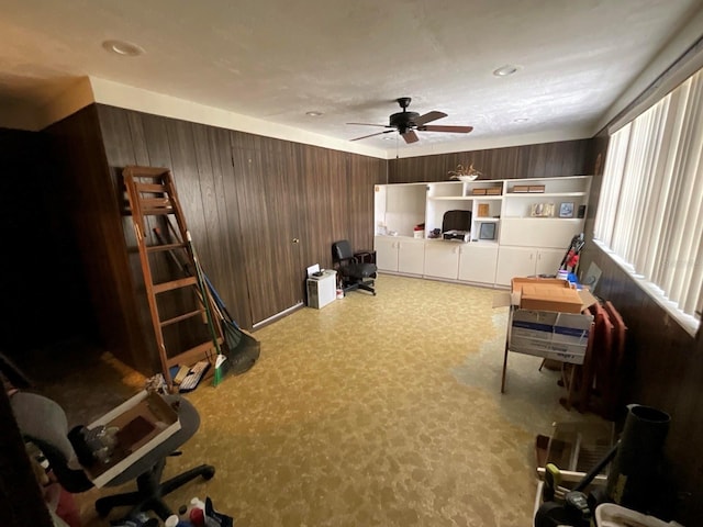 living area featuring ceiling fan, wood walls, and carpet flooring