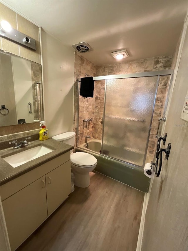 full bathroom featuring bath / shower combo with glass door, vanity, toilet, and hardwood / wood-style flooring