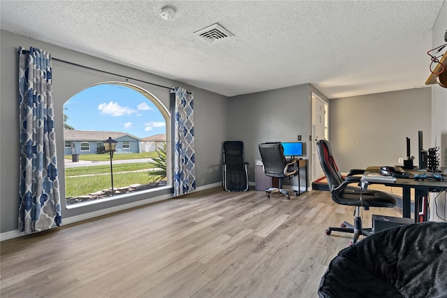 home office with a textured ceiling and light hardwood / wood-style flooring