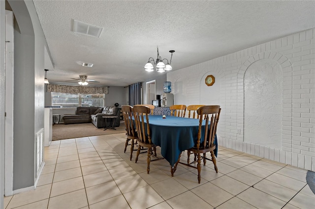 tiled dining space featuring a textured ceiling, ceiling fan with notable chandelier, and brick wall