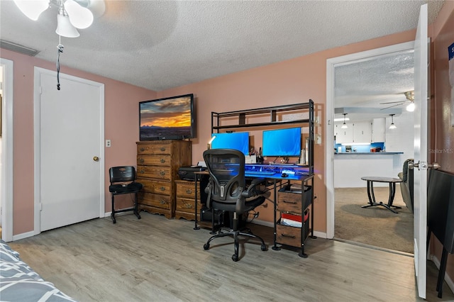 office area with a textured ceiling, ceiling fan, and light hardwood / wood-style flooring